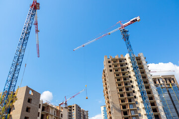 Construction cranes on the background of the blue sky at the construction site build multi-storey residential buildings