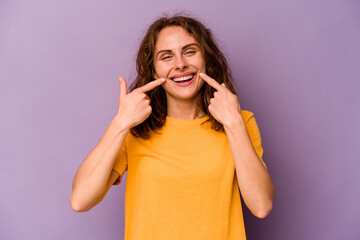 Fototapeta premium Young caucasian woman isolated on purple background smiles, pointing fingers at mouth.