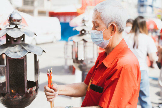 Portrait image adult 60 years old. Elderly man wearing mask to protect against toxic dust pm2.5 or virus, lighting red candle. The white-haired man is about to make wish. People wear red shirts.