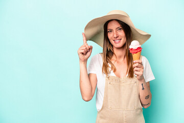 Young caucasian pregnant woman holding an ice cream isolated on blue background showing number one with finger.