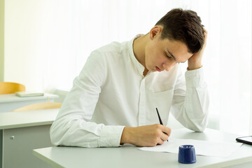 A student takes notes with a fountain pen while studying in high school while sitting at a desk. Portrait of a college guy writing with a pen while completing a task. High quality photo