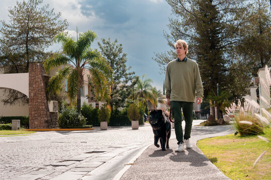 Blond Man Walking His Black Dog In His Neighborhood