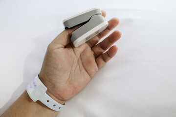 Patient on hospital bed using oximeter on thumb for measuring pulse and heart rate