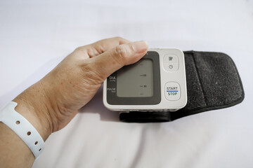 Patient's hand holding digital tensiometer on hospital bed