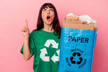 Young caucasian woman holding a recycled cardboard bag isolated on pink background pointing upside with opened mouth.