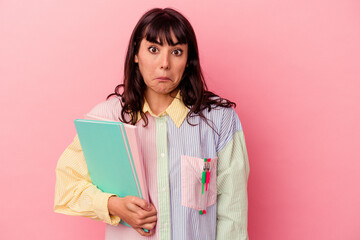 Fototapeta premium Young student caucasian woman holding books isolated on pink background shrugs shoulders and open eyes confused.
