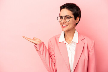 Young business woman wearing a pink blazer isolated on pink background showing a copy space on a palm and holding another hand on waist.