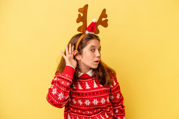 Little caucasian girl wearing a Christmas reindeer hat isolated on yellow background trying to listening a gossip.