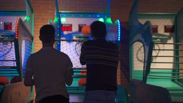 People back view Playing Basketball and Throwing Ball at Arcade Machine in Game Zone Amusement centre in Shopping mall. Two unrecognizable person have fun playing arcade machine