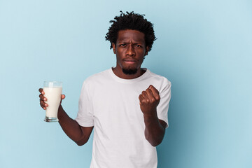 Young african american man holding a glass of milk isolated on blue background showing fist to...