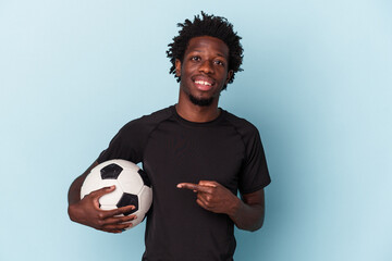 Young african american man playing soccer isolated on blue background smiling and pointing aside, showing something at blank space.