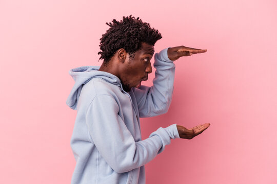 Young African American Man Isolated On Pink Background Shocked And Amazed Holding A Copy Space Between Hands.