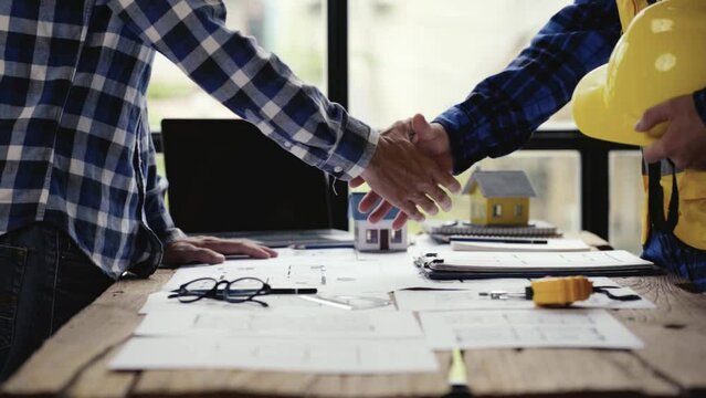Two Civil Engineer or Architect holding helmet and handshaking after a mega project done in the office construction site. engineer sketching a construction project teamwork and cooperation concept. 4k