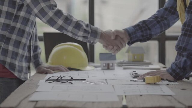 Two Civil Engineer or Architect holding helmet and handshaking after a mega project done in the office construction site. engineer sketching a construction project teamwork and cooperation concept. 4k