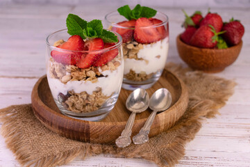 Strawberry parfait in a glass with yogurt and granola on a gray background.	
