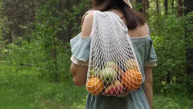 Woman walks with a braided string bag of fresh fruit. Life without plastic waste. Low-waste lifestyle. Sustainable ecological lifestyle