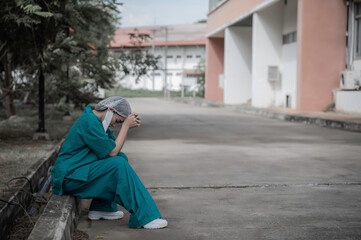 Naklejka premium Tired depressed female asian scrub nurse wears face mask blue uniform sits on hospital floor,Young woman doctor stressed from hard work