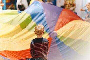 Little boy Holding Rainbow Blanket Toy and Having Fun With Other Kids. Kid at Kindergarten Playing Together