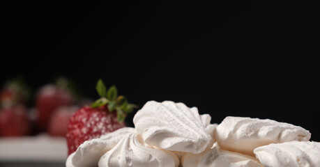 Meringue and strawberries on a black background with space for text.