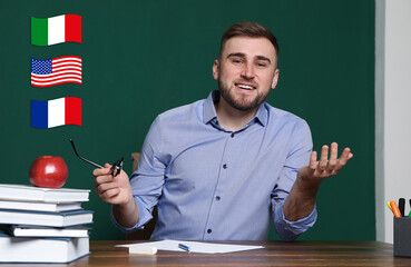 Portrait of foreign languages teacher at wooden table and different flags green chalkboard