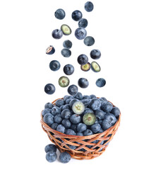 Fresh ripe blueberries falling into wicker bowl on white background