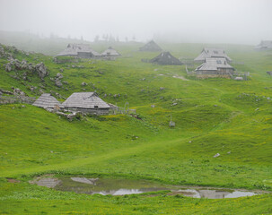 View of traditional Shepard cottages in the valley and the Alps in the background on a misty day,...