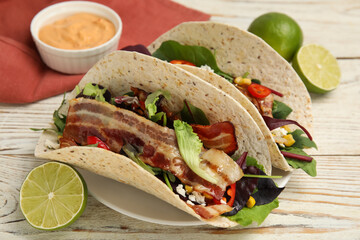Delicious tacos with fried bacon and lime on white wooden table, closeup