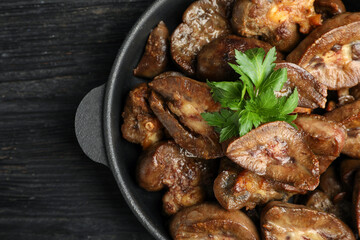 Frying pan with delicious kidneys and parsley on black wooden table, top view