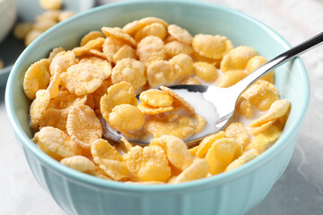 Spoon in bowl with tasty cornflakes and milk on table, closeup