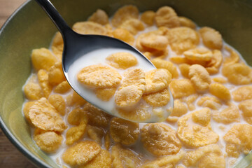 Spoon with tasty cornflakes and milk over bowl, closeup