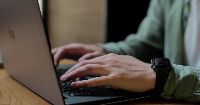 Hands of a man typing on his laptop in a coffee shop. Close up male professional researching computer scrolling social media.
