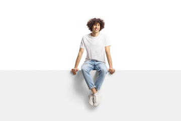 Casual young man with curly hair sitting on a panel