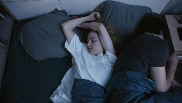 Couple sleeping in bed at night. The woman sleeps in the middle of the bed, the young man sleeps on the edge, there is not enough space for him, he wakes up and looks at the woman. Slow motion footage