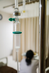 Closeup View of Infusion with Female Patient Sitting on Hospital Bed on the Background