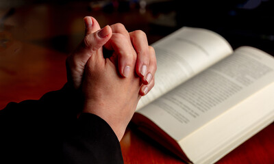 Pray to God. Female hand in prayer over a Holy Bible, wooden table, close up view.