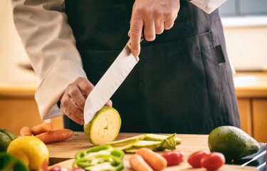 Chef cut zucchini with a knife on a chopping board, close up. Fresh vegetable on kitchen table.