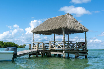 Wooden bungalow set on the water. Pavilion with thatched roof on turquoise water. Sea pier. Boat station.