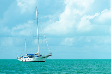 Obraz premium Lonely sailboat on a turquoise sea surface. Yacht with folded sail. Sailboat in calm weather, against the background of a cloudy sky.