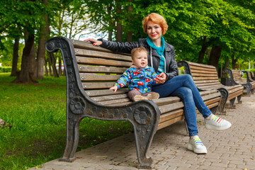 beautiful girl (mother) with a boy (son) in the park in the park are sitting on a bench