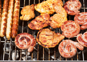 Assorted delicious grilled meat over the hot fire on a portable barbecue with steaks, sausages,...