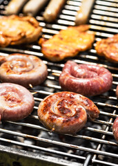 Spirals of spicy sausage grilling on a barbecue grilling over the hot coals outdoors in the garden or park on a summer picnic. Selective focus.