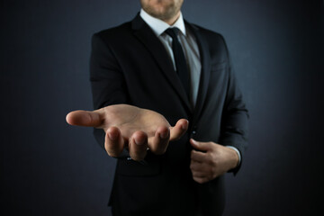 Male hand in a suit shows a palm up gesture on a black background. Concept of request, bankruptcy, close-up.
