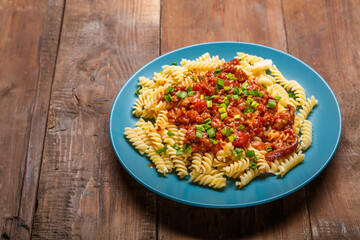 Blue plate with bolognese pasta on a wooden table sprinkled with onions.