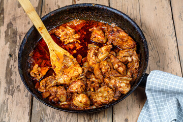 Pieces of baked chicken in sauce in a frying pan with a wooden spatula.