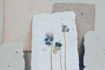 Dried viola flower pressed onto a sheet of handmade paper with a pronounced explicit texture. Reuse...