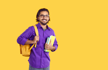 Smiling millennial Indian guy with backpack and books isolated on yellow studio background. Happy male ethnic student ready for studying abroad. International communication concept. - Powered by Adobe