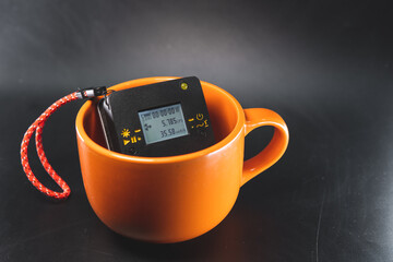 Large ceramic mug of bright orange color. Inside is a radiation dosimeter. The concept of measuring and sanitary control of health safety. Exceeding the permissible radiation