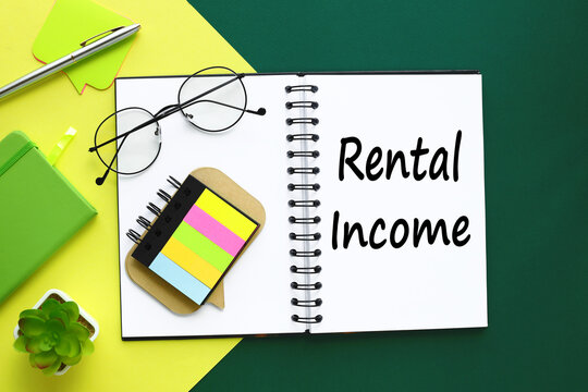 The world rental income is written in a notebook that sits on a green desktop along with a laptop. Business image