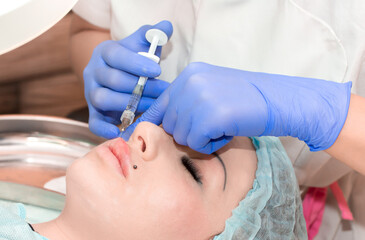 Lip augmentation. Beautician injects hyaluronic acid into the lips of a girl with a syringe. The...