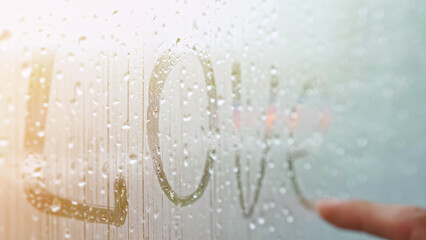 Male hand writes word Love on window glass covered with fog. Romantic inscription on misty window...